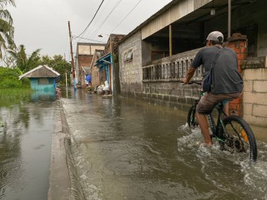 Semarang, Endonezya - 13 Mart 2024: Konut bölgesinde sel. Bisikletiyle geçen bir adam