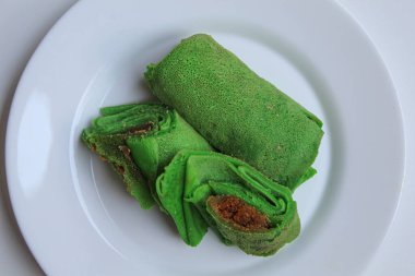 Dadar Gulung Isi Kelapa, Endonezya 'dan geleneksel tatlı. Dolgu olarak rendelenmiş hindistan cevizi ve palmiye şekerli yeşil krep. Beyaz tabakta. Beyaz arkaplan, düz yatay veya üst görünümde izole edilmiş