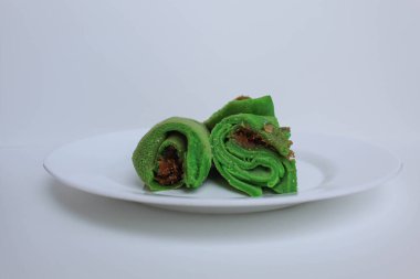 Dadar Gulung Isi Kelapa, Endonezya 'dan geleneksel tatlı. Yeşil renkli rulo krep, rendelenmiş hindistan cevizi ve kırmızı şeker. Beyaz bir plaka üzerinde, beyaz arka planda izole edilmiş.