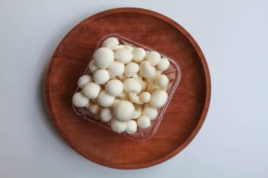 Bunapi shimeji, ya da beyaz kayın, ya da beyaz istiridye kabuklu mantar, ahşap tabakta, beyaz zemin üzerinde, düz ya da üst görünüm