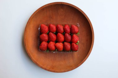 Plastik kabın içinde, tahta tabakta, beyaz arka planda, düz yerde ya da üst tarafta taze çilekler var.