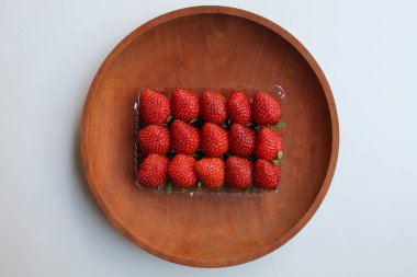 Plastik kabın içinde, tahta tabakta, beyaz arka planda, düz yerde ya da üst tarafta taze çilekler var.