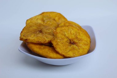 Küçük beyaz tabak üzerinde dilimlenmiş muz sikkeleri, beyaz arka planda izole edilmiş.