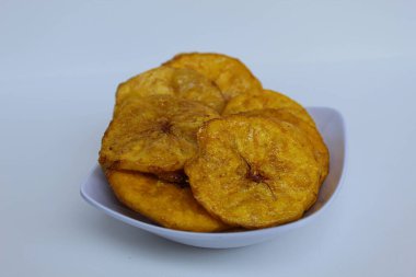 Küçük beyaz tabak üzerinde dilimlenmiş muz sikkeleri, beyaz arka planda izole edilmiş.