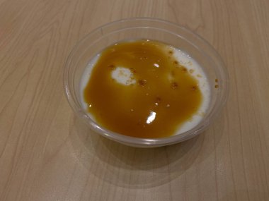 Karamel soslu vanilyalı puding şeffaf plastik kasede, ahşap masanın üzerinde.