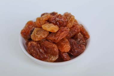 Beyaz arka planda izole edilmiş küçük beyaz bir kâse içinde kuru üzüm yığını.