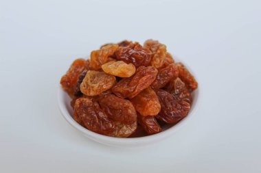 Beyaz arka planda izole edilmiş küçük beyaz bir kâse içinde kuru üzüm yığını.