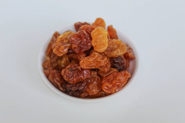 Beyaz arka planda izole edilmiş küçük beyaz bir kâse içinde kuru üzüm yığını.