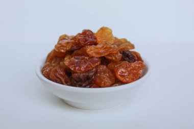 Beyaz arka planda izole edilmiş küçük beyaz bir kâse içinde kuru üzüm yığını.