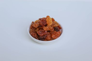 Beyaz arka planda izole edilmiş küçük beyaz bir kâse içinde kuru üzüm yığını.