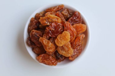 Beyaz zemin üzerinde izole edilmiş, küçük beyaz bir kasede kuru üzüm yığını.