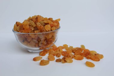 Şeffaf bir kaseden taşan kuru üzümler, dağınık, izole beyaz arka plan