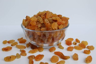 Şeffaf bir kaseden taşan kuru üzümler, dağınık, izole beyaz arka plan