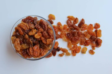 Şeffaf bir kaseden taşan kuru üzümler, dağınık, izole beyaz arka plan, düz ya da üst görünüm