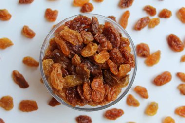 Şeffaf kâsenin etrafına saçılmış kuru üzümler, izole edilmiş beyaz arka plan, düz ya da üst görünüm