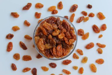 Şeffaf kâsenin etrafına saçılmış kuru üzümler, izole edilmiş beyaz arka plan, düz ya da üst görünüm