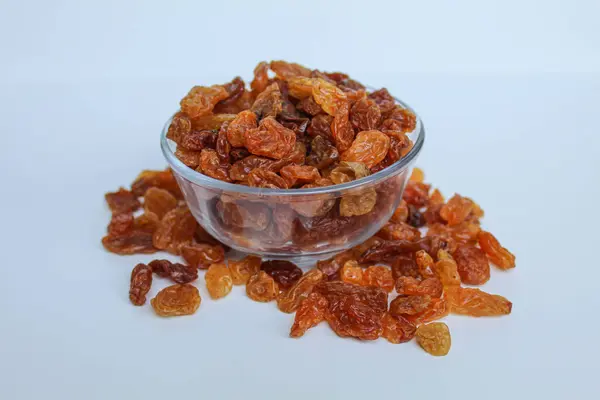 Şeffaf bir kaseden taşan kuru üzümler, dağınık, izole beyaz arka plan