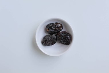 Üç parça ajwa hurması ya da ajwa khajur, küçük kasede, beyaz arka planda izole edilmiş, düz ya da üst görünümde.
