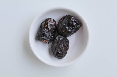 Üç parça ajwa hurması ya da ajwa khajur, küçük kasede, beyaz arka planda izole edilmiş, düz ya da üst görünümde.
