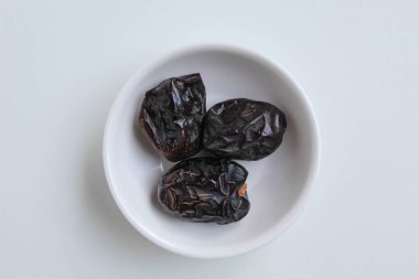 Üç parça ajwa hurması ya da ajwa khajur, küçük kasede, beyaz arka planda izole edilmiş.