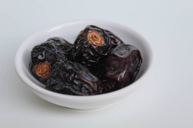 Beş parça ajwa hurması ya da ajwa khajur, küçük kasede, beyaz arka planda izole edilmiş.