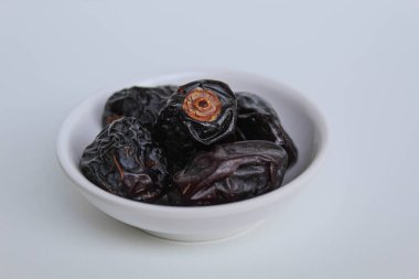 Beş parça ajwa hurması ya da ajwa khajur, küçük kasede, beyaz arka planda izole edilmiş.
