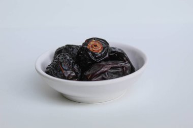 Beş parça ajwa hurması ya da ajwa khajur, küçük kasede, beyaz arka planda izole edilmiş.