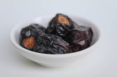 Beş parça ajwa hurması ya da ajwa khajur, küçük kasede, beyaz arka planda izole edilmiş.