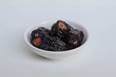 Beş parça ajwa hurması ya da ajwa khajur, küçük kasede, beyaz arka planda izole edilmiş.