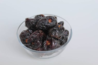Ajwa tarihleri ya da ajwa hajur, şeffaf kâsede, beyaz arka planda izole edilmiş.