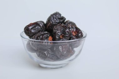 Ajwa tarihleri ya da ajwa hajur, şeffaf kâsede, beyaz arka planda izole edilmiş.