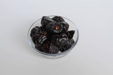 Ajwa tarihleri ya da ajwa hajur, şeffaf kâsede, beyaz arka planda izole edilmiş.