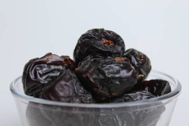 Ajwa tarihleri ya da ajwa hajur, şeffaf kâsede, beyaz arka planda izole edilmiş.