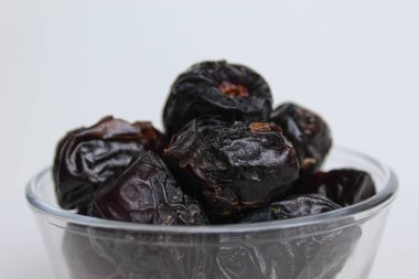 Ajwa tarihleri ya da ajwa hajur, şeffaf kâsede, beyaz arka planda izole edilmiş.