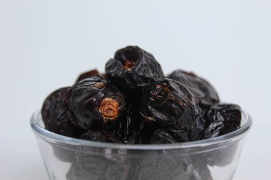 Ajwa tarihleri ya da ajwa hajur, şeffaf kâsede, beyaz arka planda izole edilmiş.