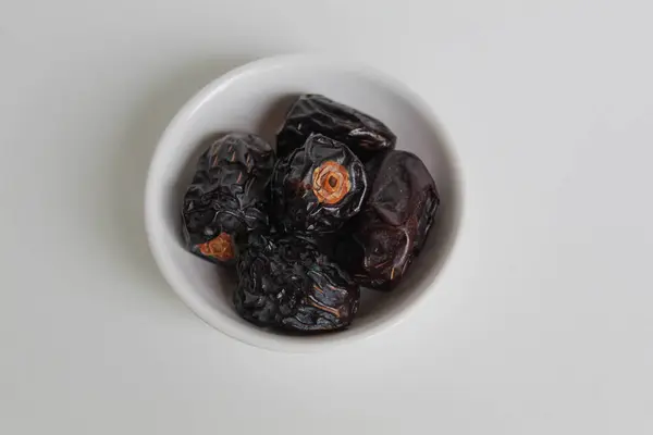 Beş parça ajwa hurması ya da ajwa khajur, küçük kasede, beyaz arka planda izole edilmiş.