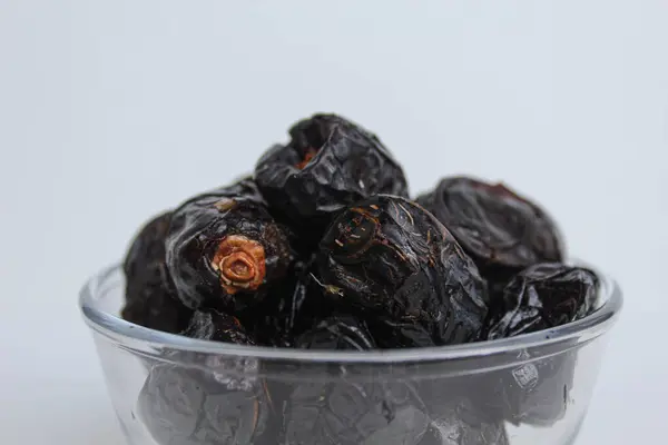 Ajwa tarihleri ya da ajwa hajur, şeffaf kâsede, beyaz arka planda izole edilmiş.