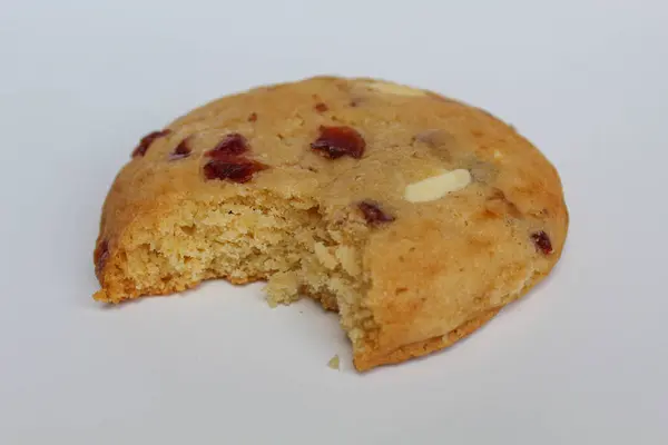 Beyaz arka planda izole edilmiş badem ve böğürtlen kesikli ısırılmış beyaz çikolatalı kurabiye.