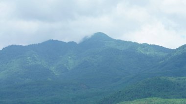 Güzel dağlar bulutlu gökyüzü ve aralarında vadi ile görünür.