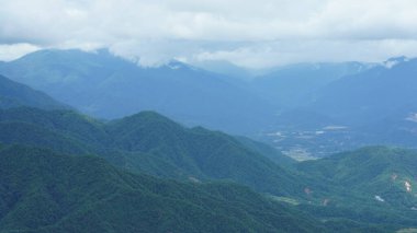 Güzel dağlar bulutlu gökyüzü ve aralarında vadi ile görünür.