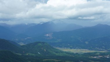 Arkaplanı bulutlu gökyüzü olan dağların arasındaki vadide bulunan sarı pirinç tarlası manzarası.