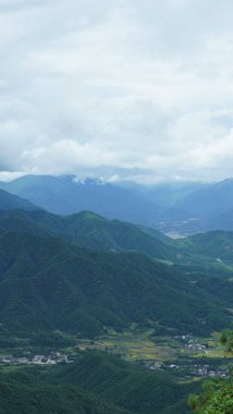 Güzel dağlar bulutlu gökyüzü ve aralarında vadi ile görünür.