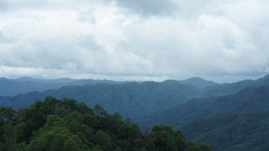 Güzel dağlar bulutlu gökyüzü ve aralarında vadi ile görünür.