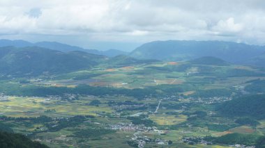 Arkaplanı bulutlu gökyüzü olan dağların arasındaki vadide bulunan sarı pirinç tarlası manzarası.