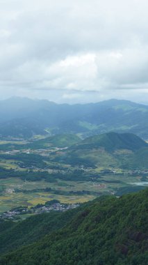 Arkaplanı bulutlu gökyüzü olan dağların arasındaki vadide bulunan sarı pirinç tarlası manzarası.