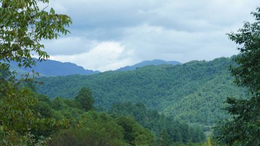 Güzel dağlar bulutlu gökyüzü ve aralarında vadi ile görünür.