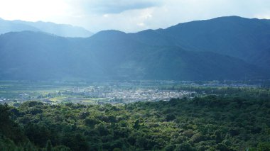 Arkaplanı bulutlu gökyüzü olan dağların arasındaki vadide bulunan sarı pirinç tarlası manzarası.