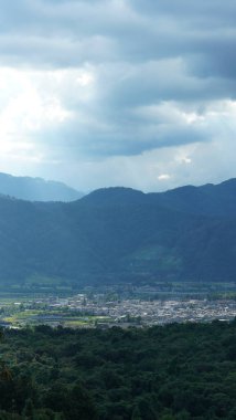 Arkaplanı bulutlu gökyüzü olan dağların arasındaki vadide bulunan sarı pirinç tarlası manzarası.