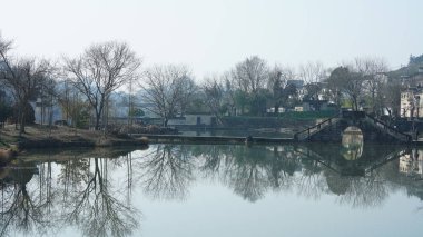 Çin 'in güney kırsalında eski kemerli taş köprüsü ve eski ahşap binaları olan geleneksel bir Çin köyü manzarası.
