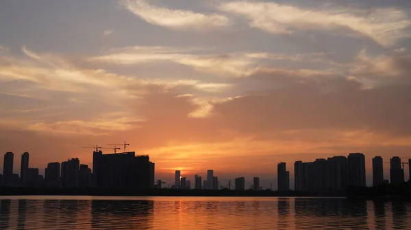 stock image The beautiful sunset view with the buildings' silhouette and orange color sky mirrored in the peaceful lake in the city